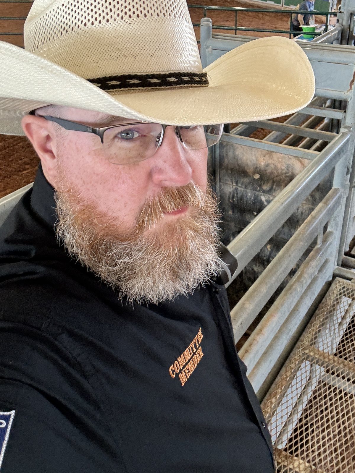 Joshua Morris in a committee member shirt beside the bucking chutes at a rodeo